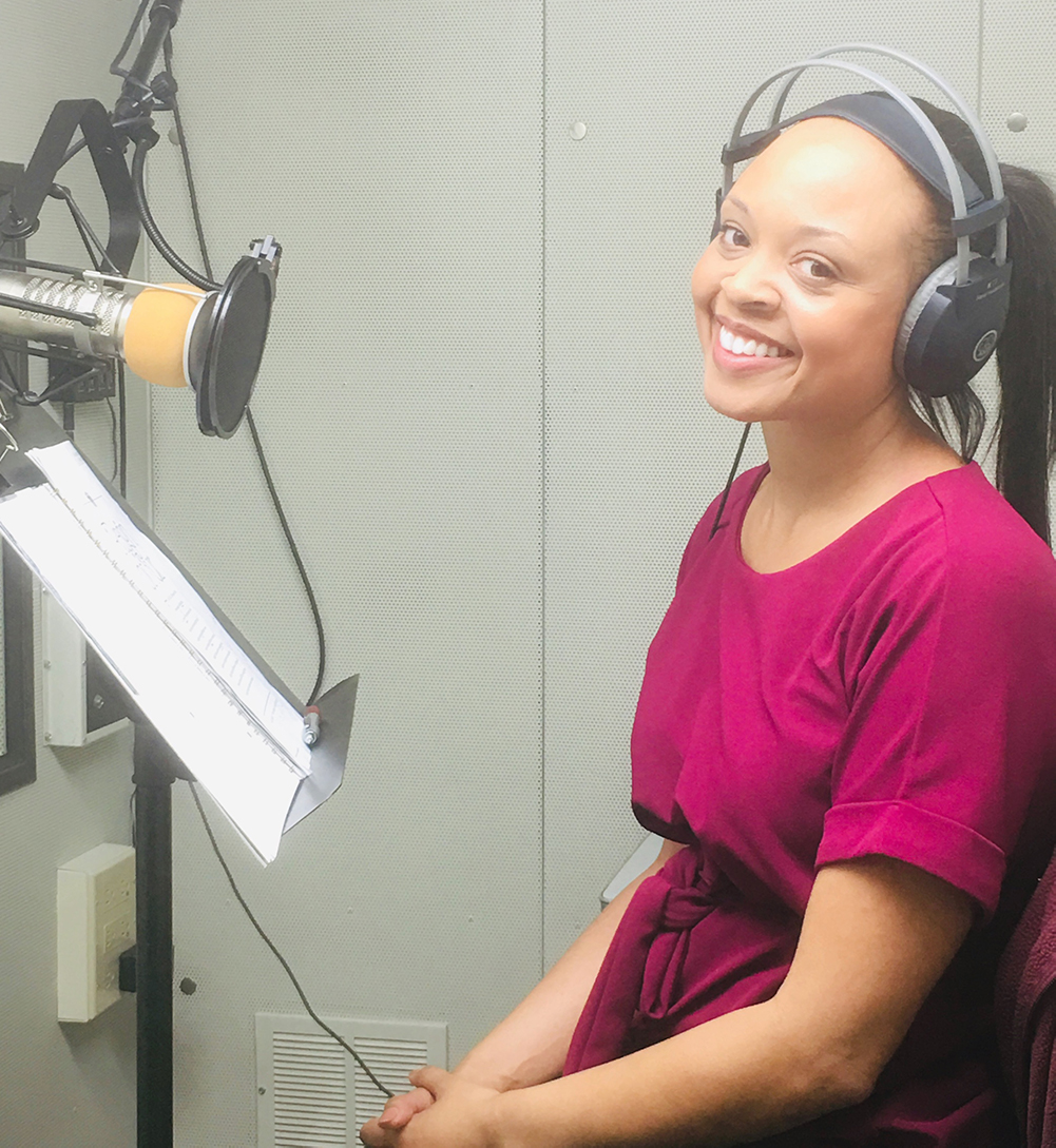 A female volunteer with headphones on sits in front of a microphone in the recording booth.